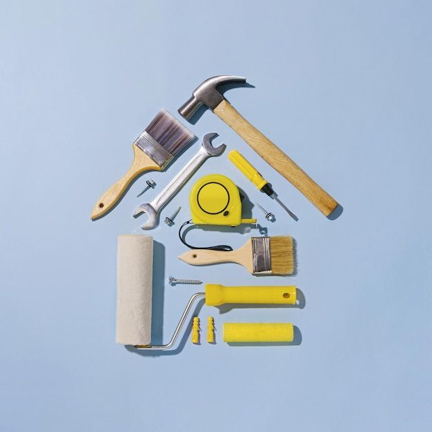 Creative flat lay still life with an assortment of household tools forming a small house in a diy, renovations, construction or maintenance concept over blue | Premium Photo